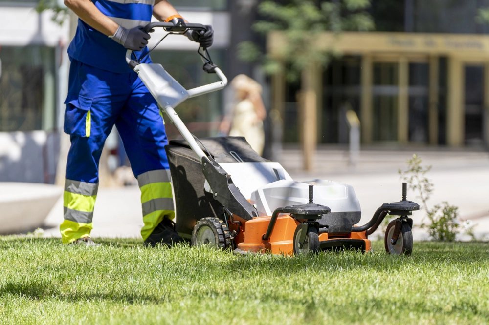 Koszenie trawników – pracownik ogrodowy koszący trawnik kosiarką spalinową w miejskiej przestrzeni zielonej